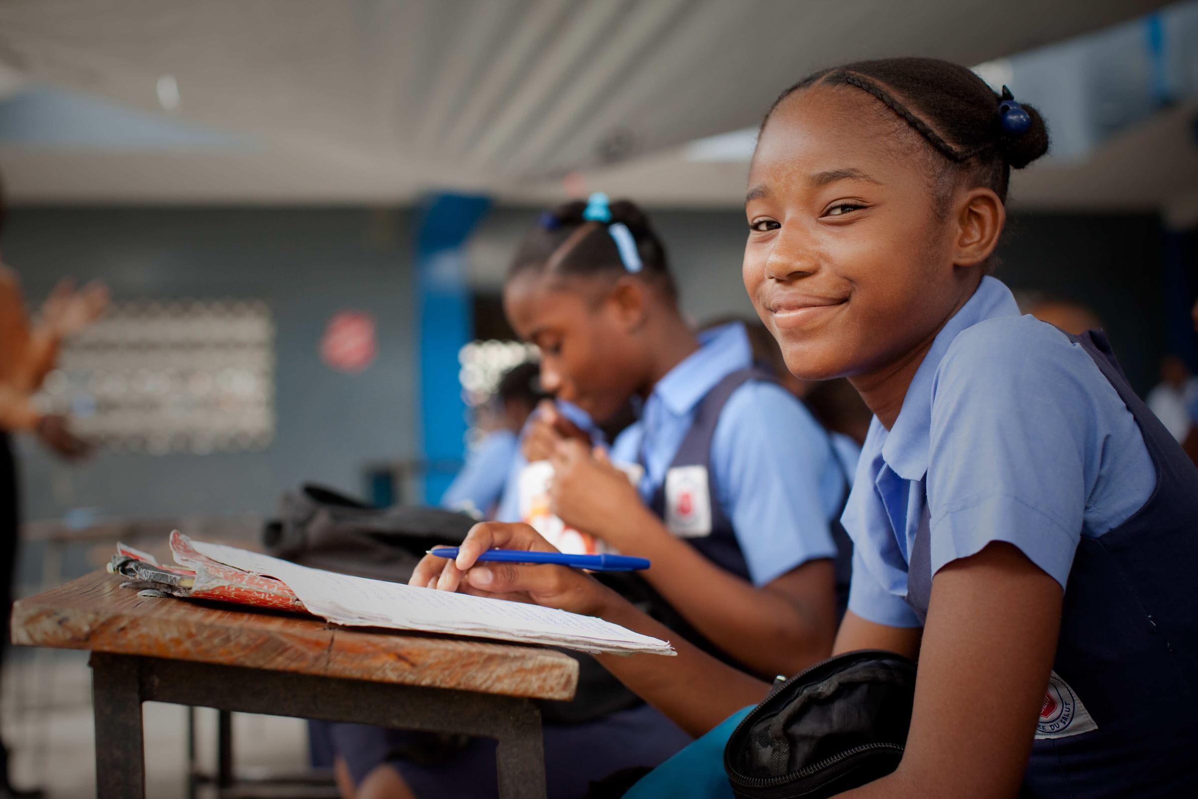 Mädchen sitzt in Schuluniform in einem Klassenraum und lächelt. (Quelle: Kpindernothilfe)