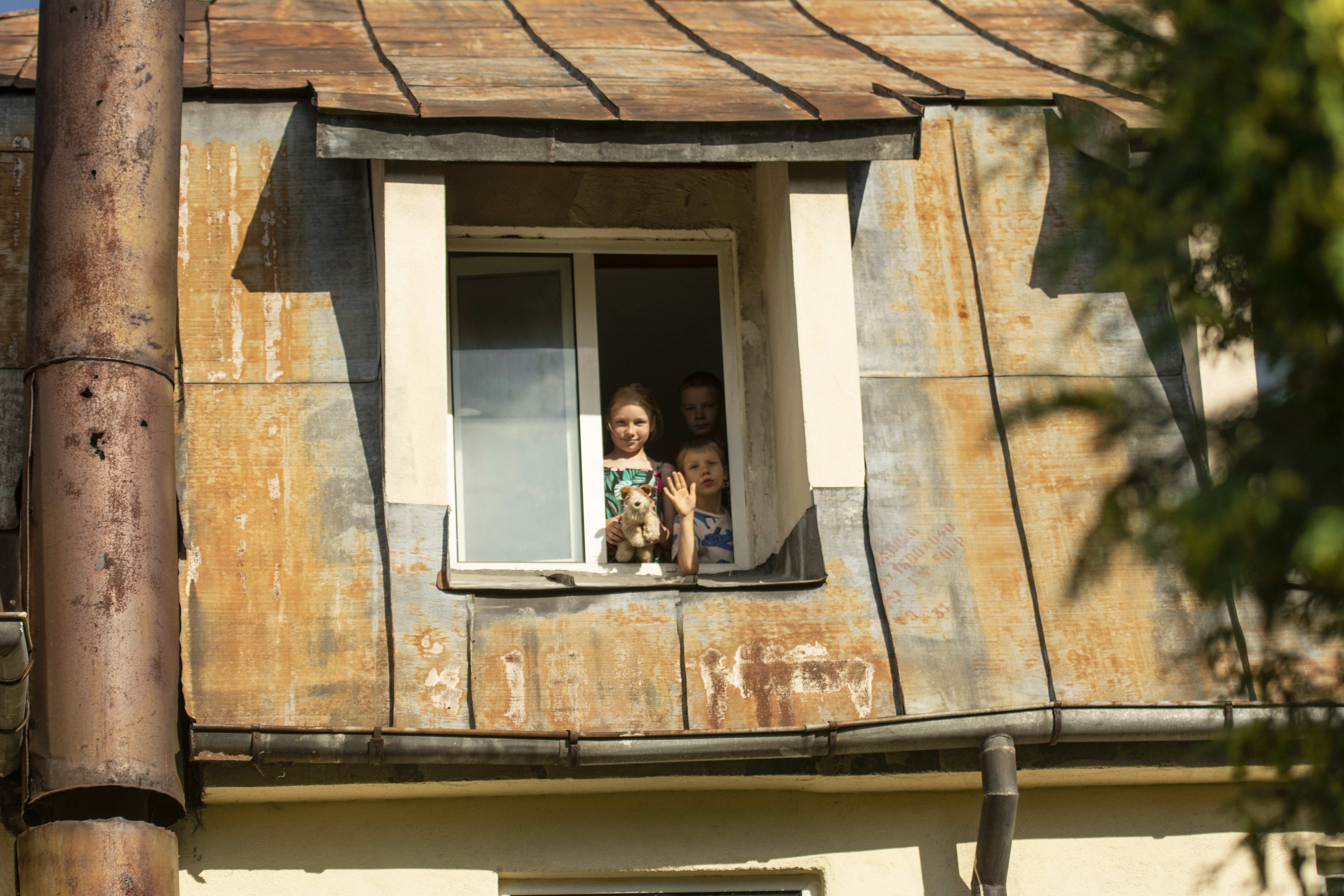Margot und ein Junge schauen aus einem Dachfenster und winken (Quelle: Christian Nusch)