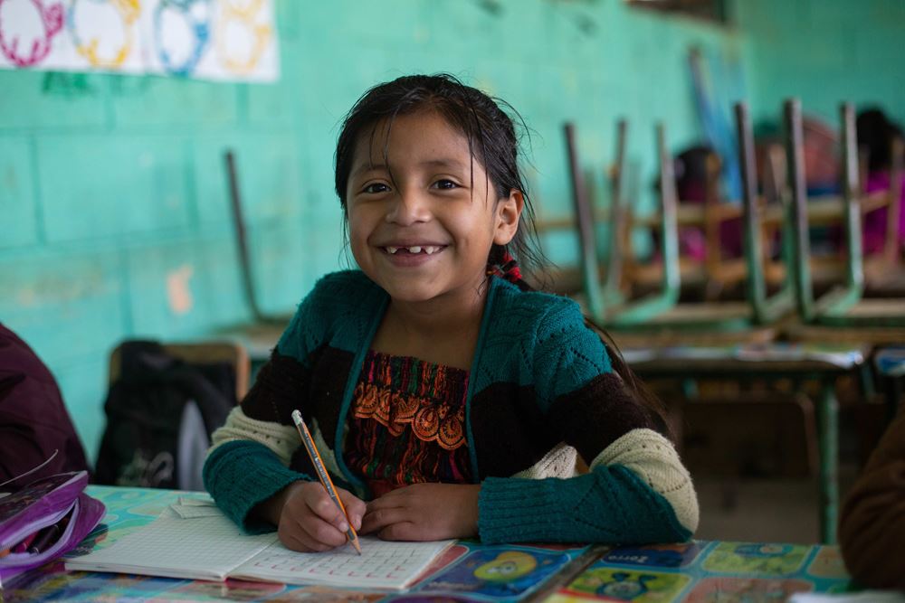 Ein Mädchen aus Guatemala sitzt in der Schule in de ersten Reihe und lernt. (Quelle: Jakob Studnar) Eine Schulklasse in Guatemala. Mädchen aus der ersten Reihe lächelt in die Kamera. (Quelle: Jakob Studnar)