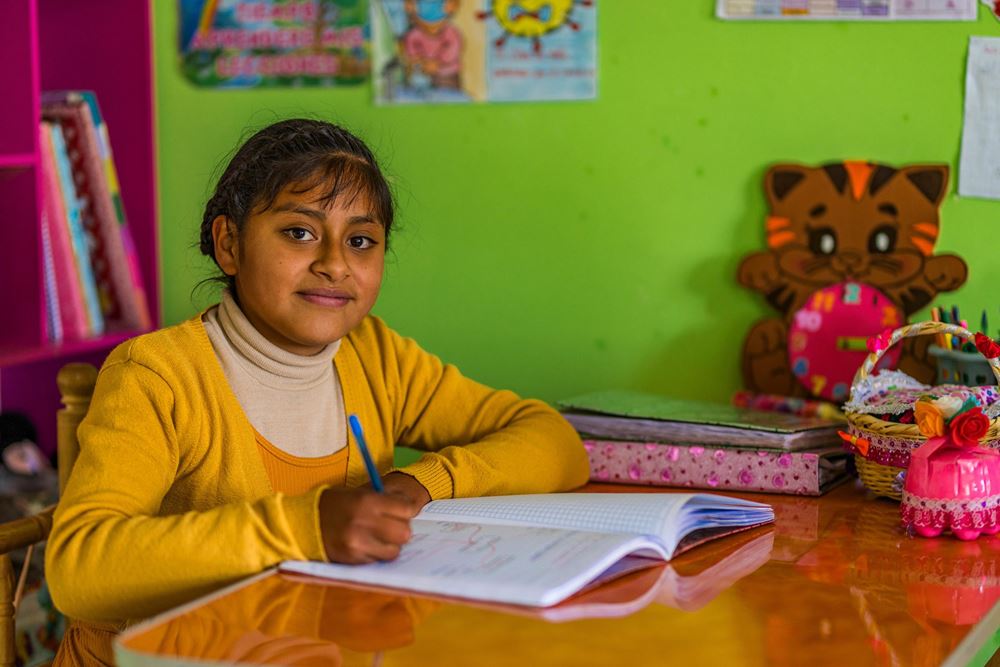Ein Mädchen aus Peru schaut in die Kamera und schreibt etwas in ein Heft (Foto: Martin Bondzio) Ein Mädchen aus Peru schaut in die Kamera und schreibt etwas in ein Heft (Foto: Martin Bondzio)