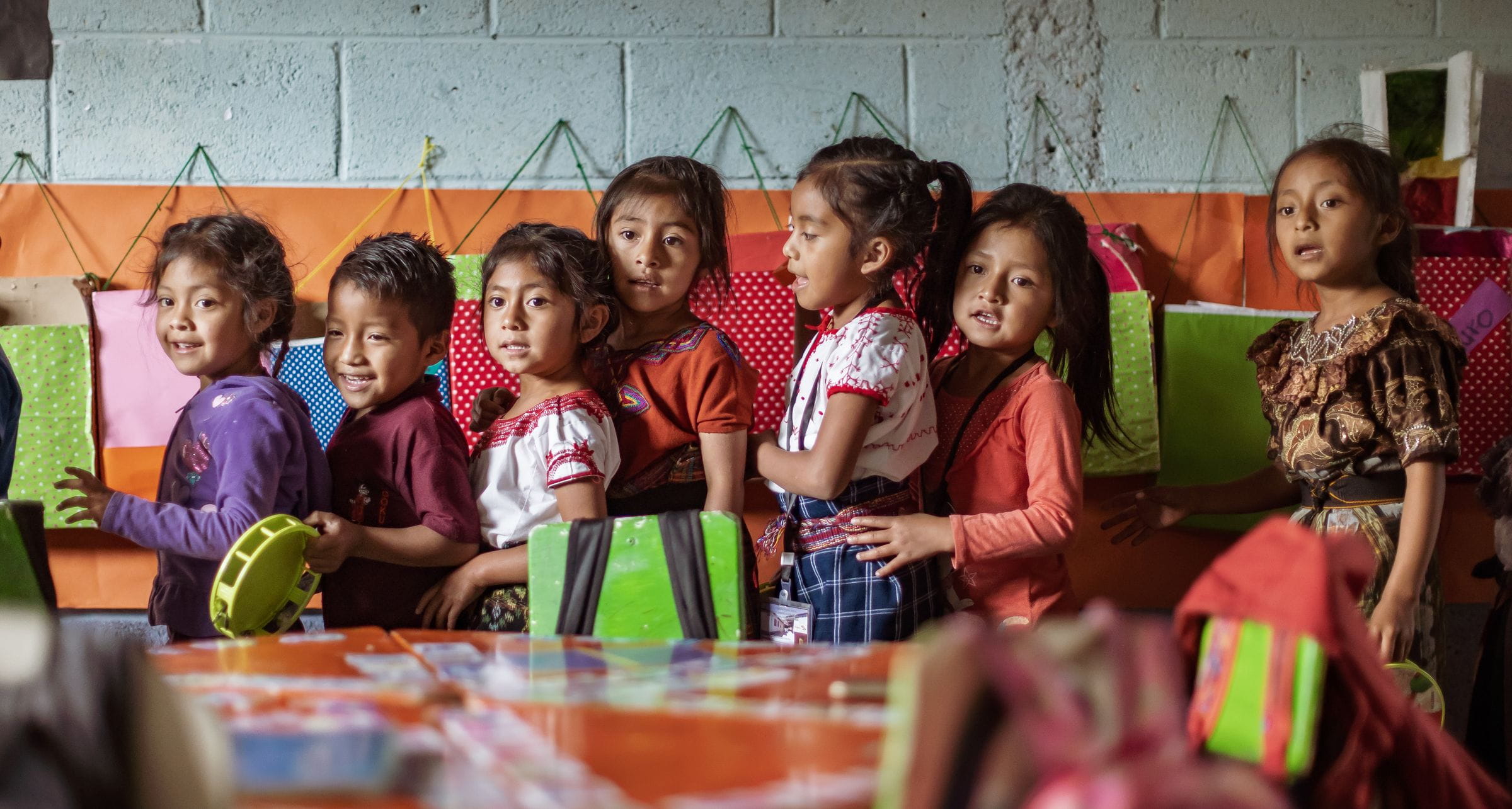 Kinder aus Guatemala stehen hintereinander in ihrem bunten Klassenraum. (Quelle: Jakob Studnar)