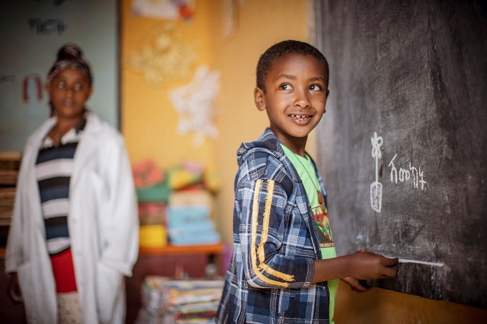 Eine Junge aus Äthiopien steht lachend an der Tafel. (Quelle: Jakob Studnar)
